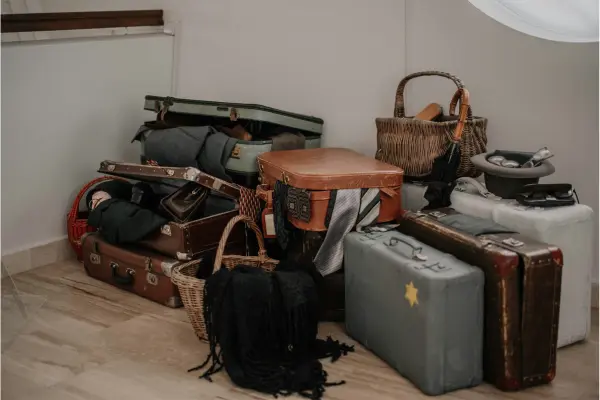 A collection of packed suitcases, travel bags, and woven baskets placed on the floor, ready for shipment or travel, representing unaccompanied baggage preparation.