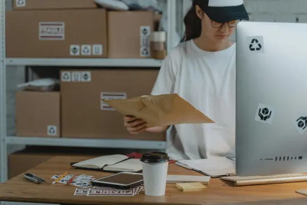 Warehouse staff member reviewing shipping documents at a desk with parcels and labels, illustrating eCommerce order processing, parcel handling, and logistics operations.