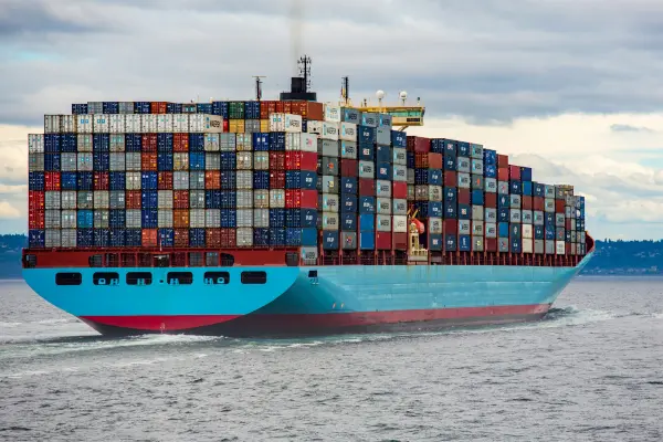 Large container ship carrying stacked shipping containers at sea, representing international freight shipping and global logistics operations.